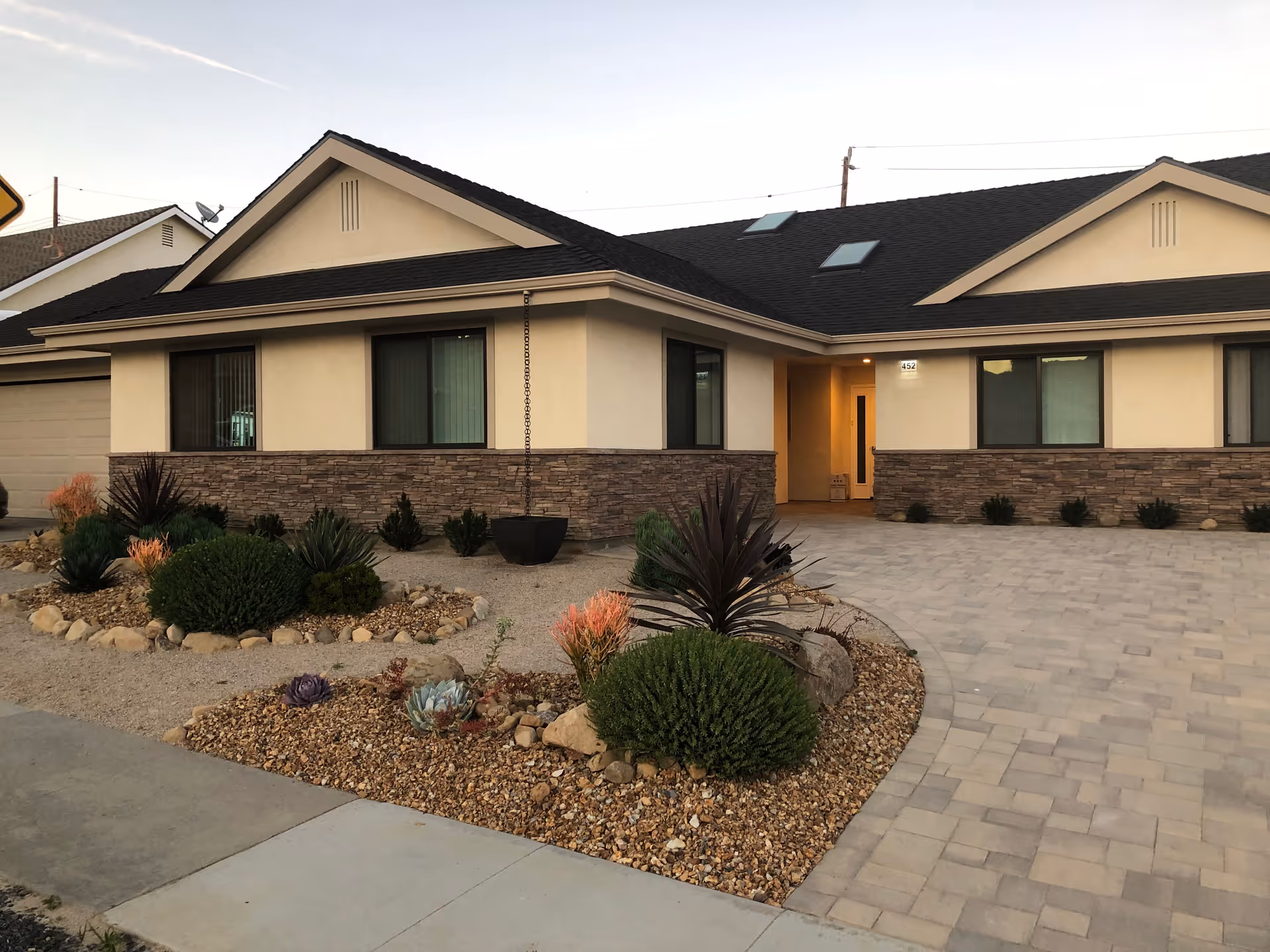 Single-story beige building with a stone facade, landscaped rock garden, and a paved driveway in front.