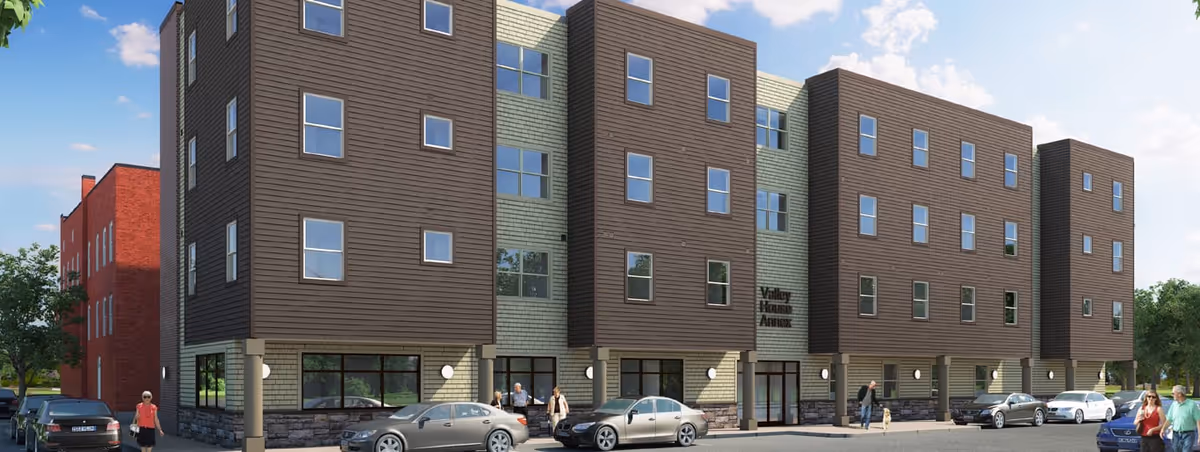 Exterior view of a modern four-story residential building named Valley House Annex with multiple windows, parked cars in front, and people walking on the sidewalk under a partly cloudy sky.