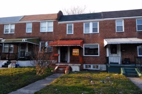 Row of brick townhouses with awnings and small front lawns.