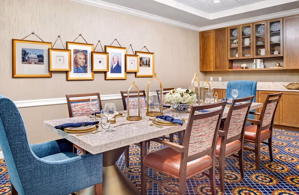 Elegantly set dining room with a marble table, upholstered chairs, framed artwork on the wall, and built-in cabinetry.
