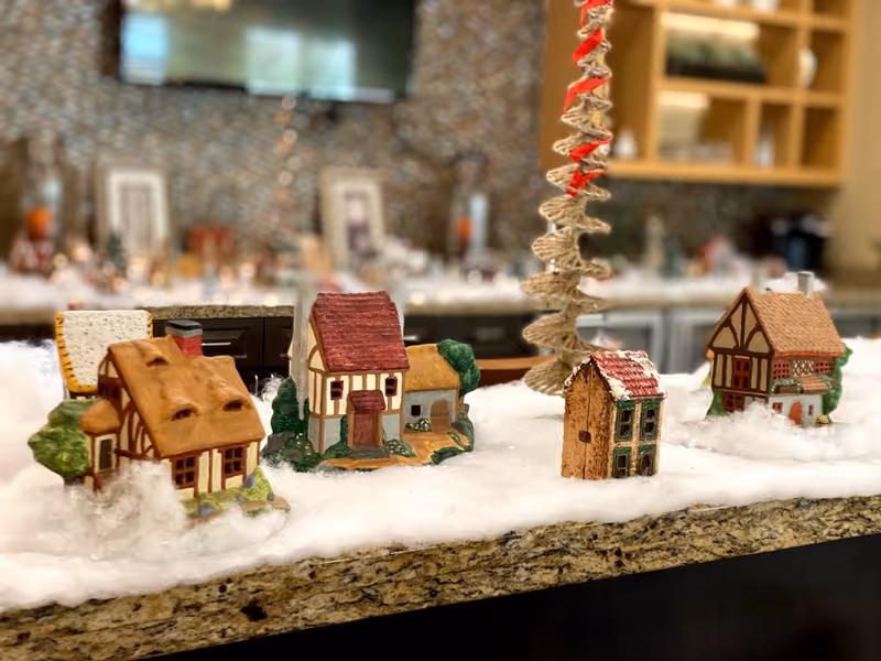 Miniature model houses arranged on faux snow on a granite counter in a decorated indoor communal space.