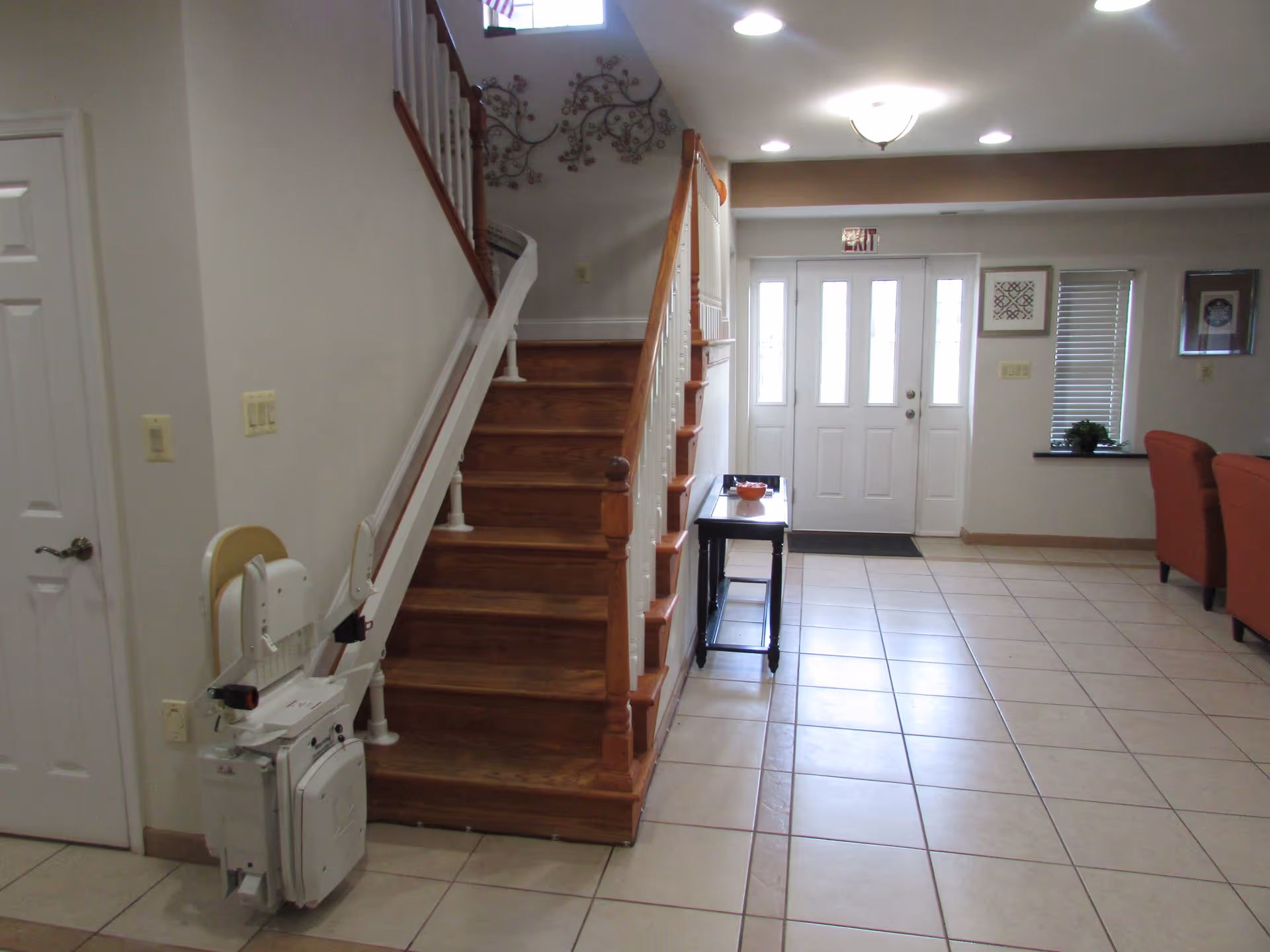 Bright lobby area with wooden staircase, stairlift, front door, and seating.