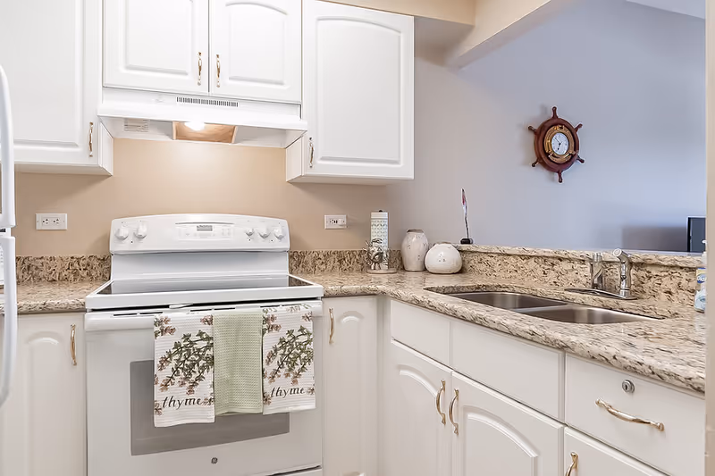 Bright white kitchen with an electric range, granite countertops, double sink, and white cabinetry.