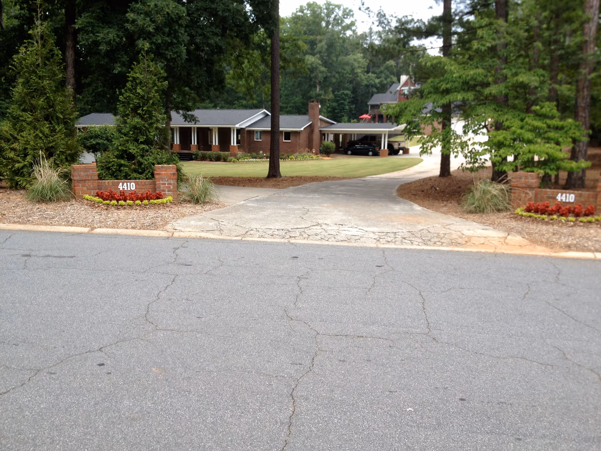 View of the entrance driveway to a single-story brick building surrounded by trees and landscaping, with two brick pillars on either side displaying the number 4410.
