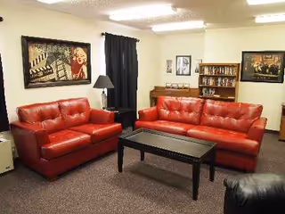 Red leather sofas, a coffee table, and bookshelves fill a cozy senior living lounge.
