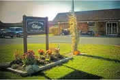 Outdoor view of Christian Park Village facility with a sign displaying the name, a landscaped area with flowers and a tall corn stalk decoration, and a brick building in the background under a clear sky.