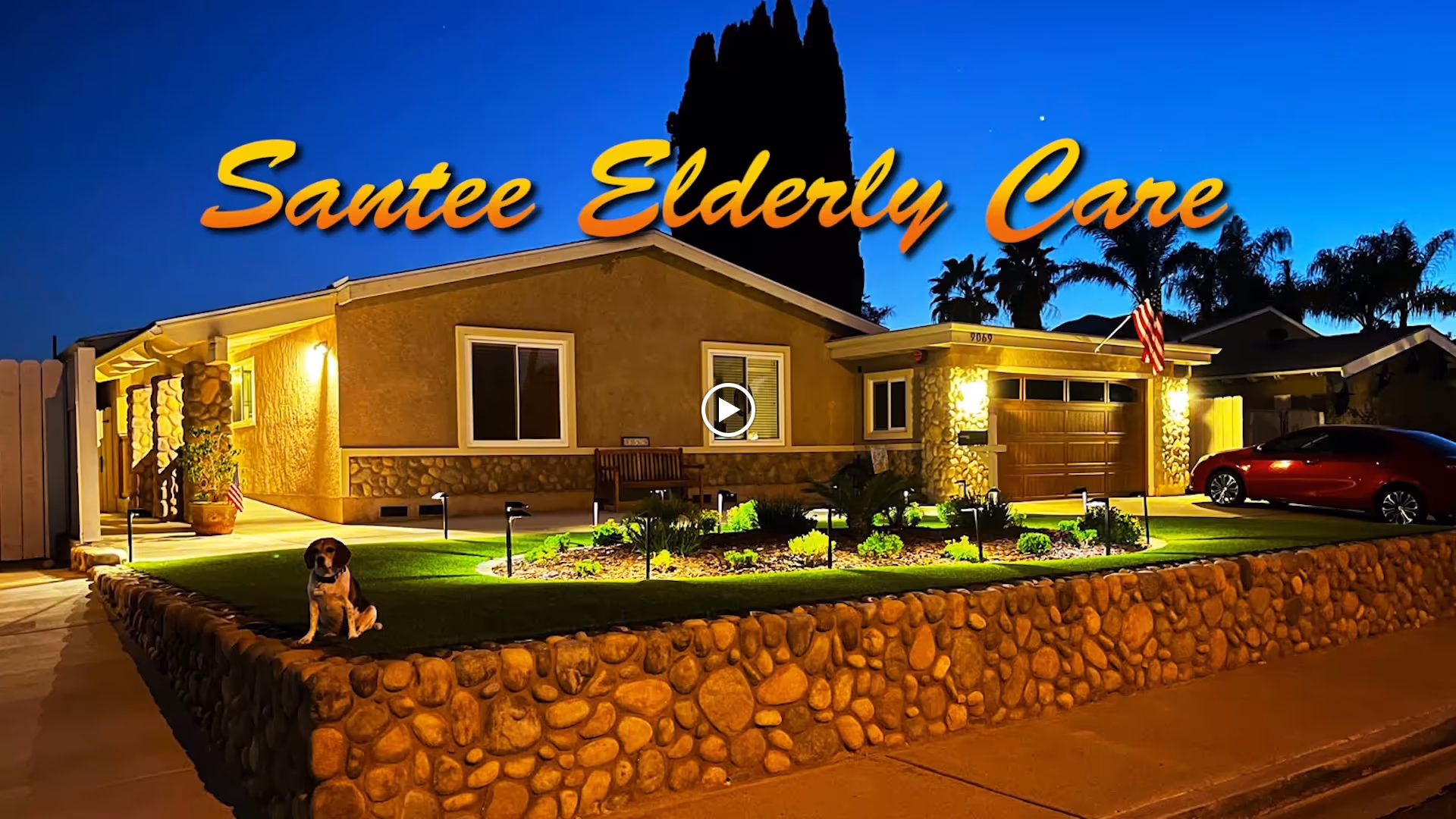 Nighttime front view of a single-story house with illuminated yard, a dog on a stone-bordered lawn, and the text 'Santee Elderly Care' across the sky.