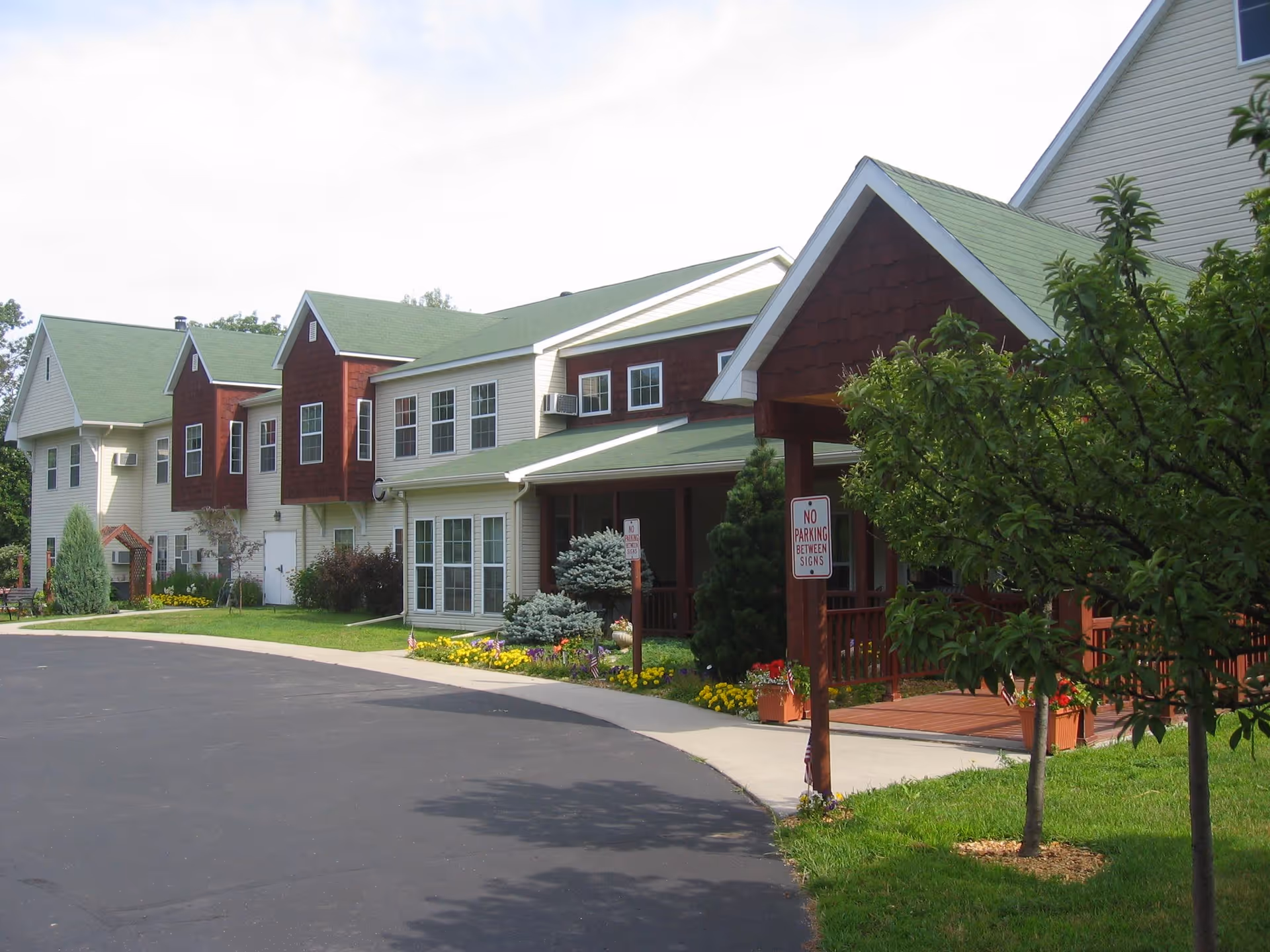 Front exterior of a multi-unit senior living building with green roofs, a covered porch entrance, landscaping and a curved driveway.