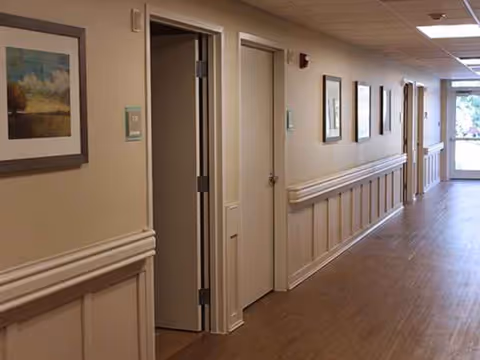 Narrow hallway in a senior living facility with framed art along beige walls.