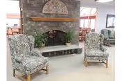 Two floral armchairs flank a brick fireplace in a senior living lounge.