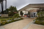Entrance to Garden View Post-Acute Rehab facility with a covered driveway, surrounded by landscaped gardens with various plants and flowers under an overcast sky.