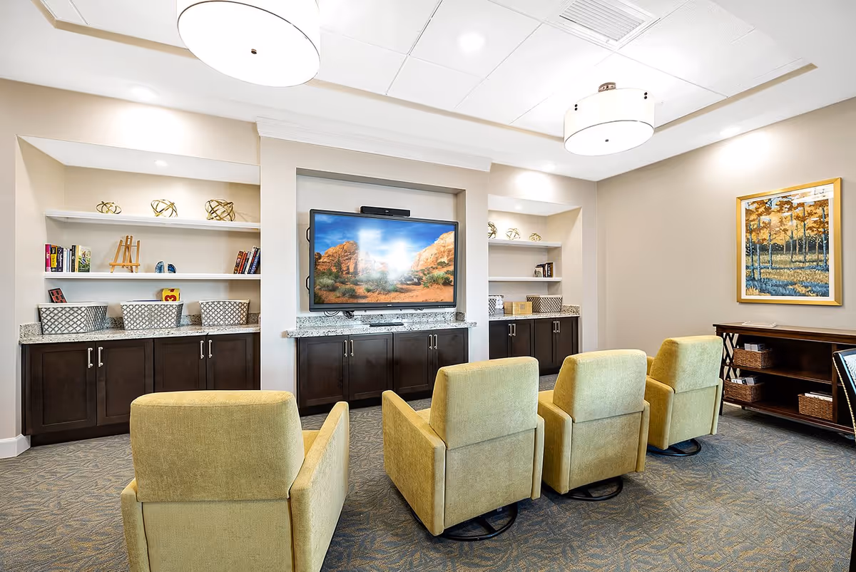 A cozy lounge with four upholstered chairs facing a wall-mounted TV and built-in shelves and cabinets.