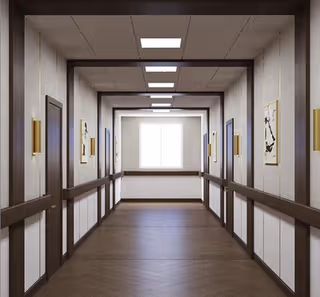 Well-lit interior hallway with handrails, doors on either side, framed artwork, and a window at the far end.