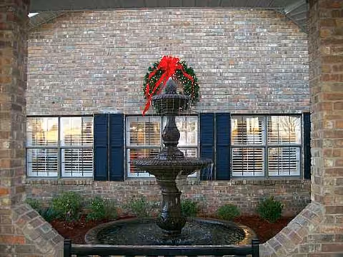 Brick courtyard featuring a tiered fountain and a red flower basket above.