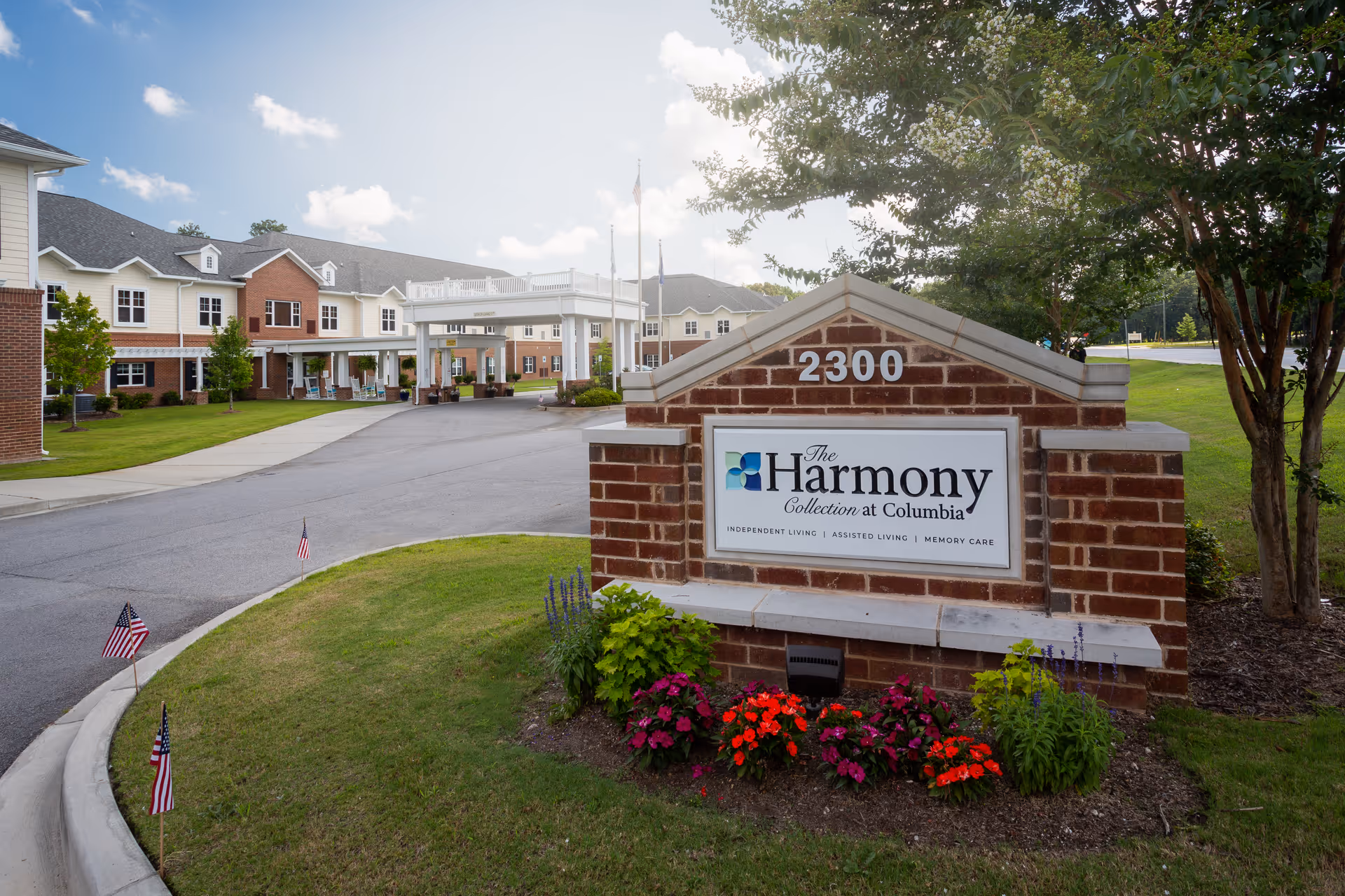 Brick entrance sign reading 'The Harmony Collection at Columbia' and '2300' in front of a landscaped driveway and the facility building.