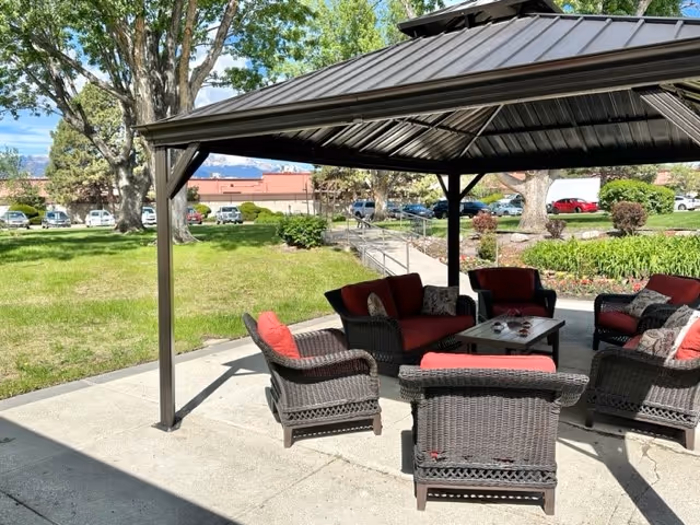 Outdoor covered seating area with wicker chairs and red cushions under a gazebo on a lawn.