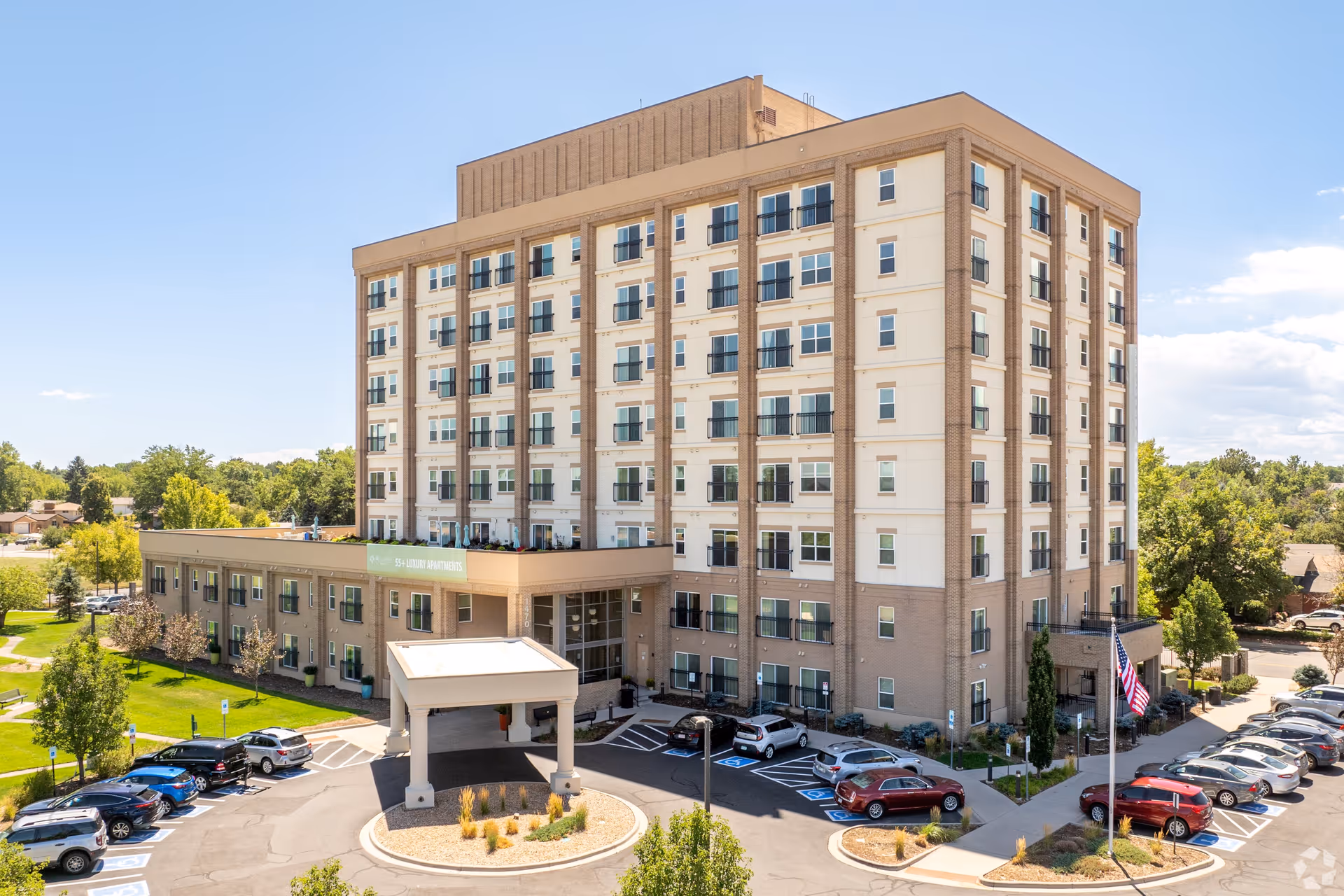 Exterior view of a multi-story senior living facility named Bella Vita with a parking lot in front, surrounded by trees and greenery under a clear blue sky.
