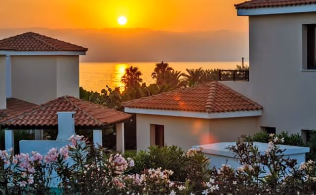 Sunset over a courtyard of white buildings with red-tiled roofs and flowering bushes