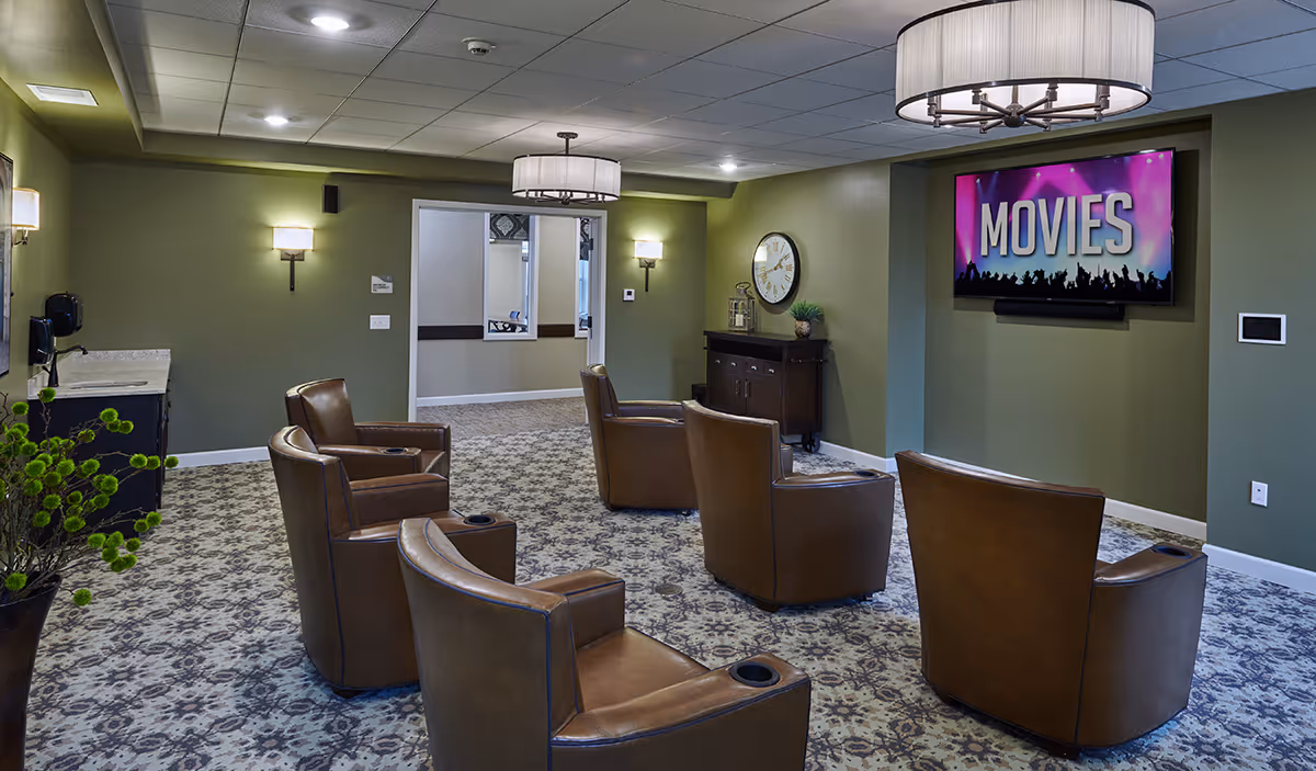 A communal media room with leather armchairs arranged facing a wall-mounted TV displaying 'MOVIES'.