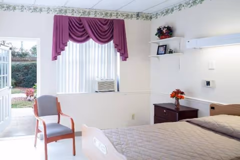 Bright bedroom featuring a bed, chair, nightstand, window with purple drapes, and a window air conditioner.