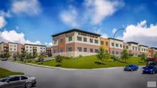 Exterior view of a multi-story senior living building on a grassy slope with cars on the street under a blue sky.