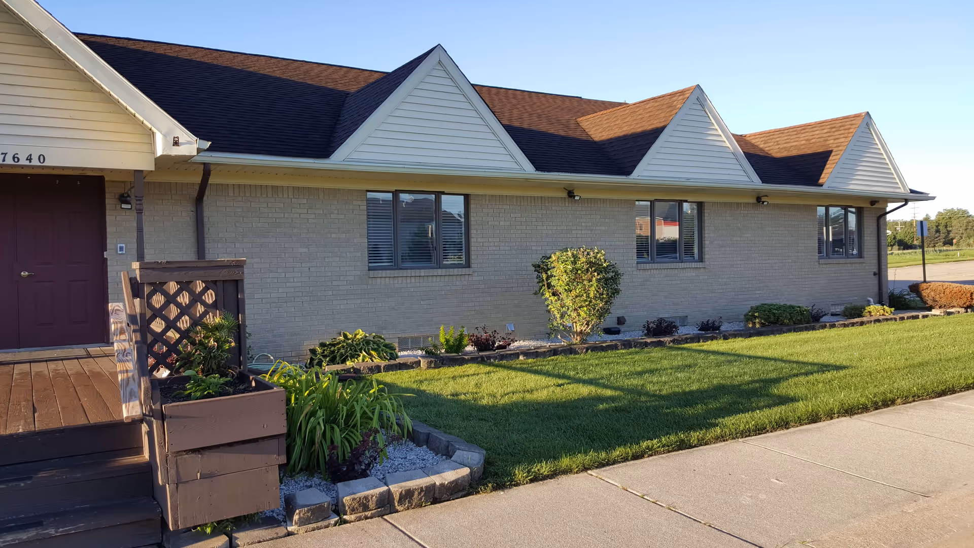 Front exterior of a one-story brick building with a small wooden porch, lawn, and landscaped beds.