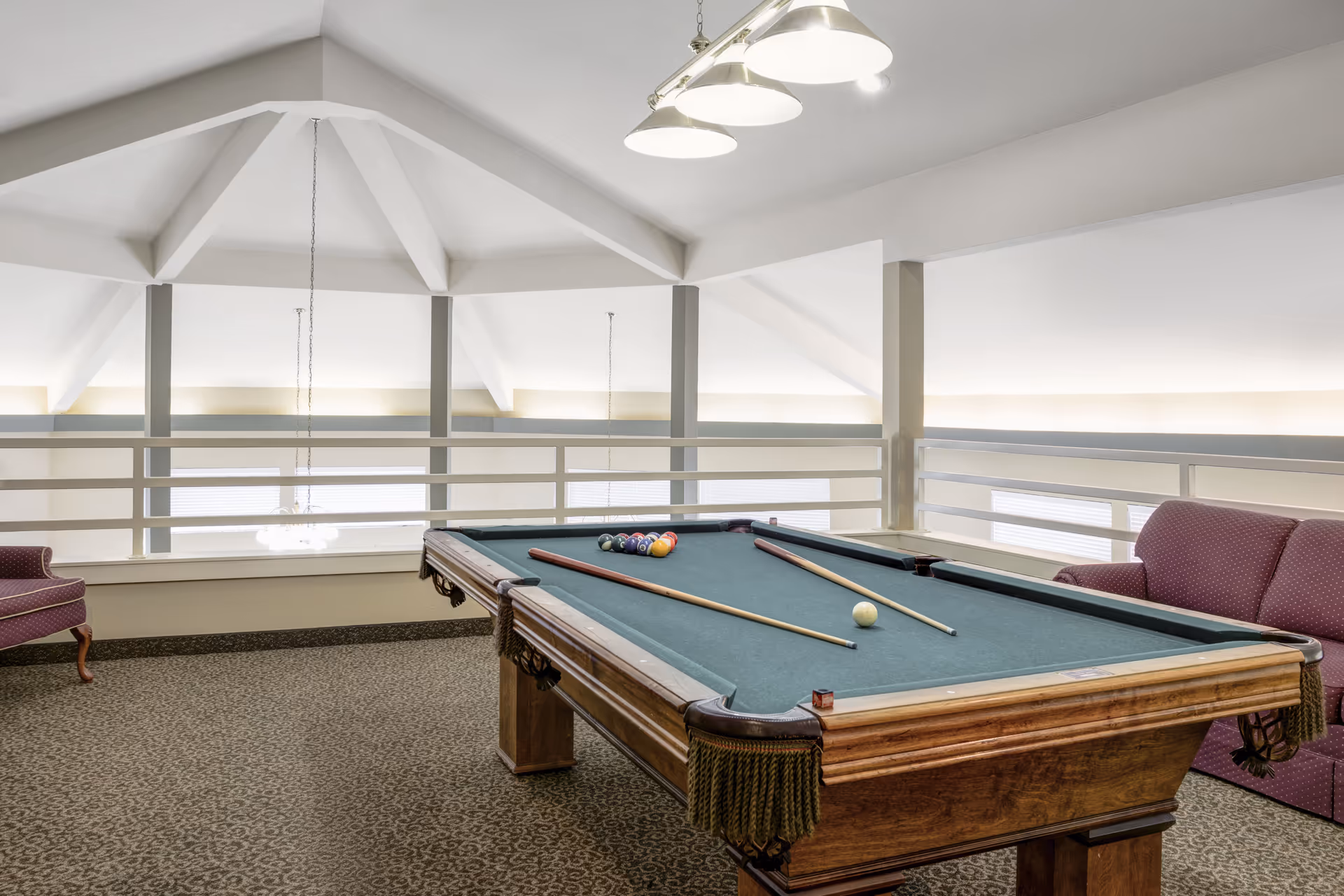 An interior lounge area with a pool table, cues and seating beneath a vaulted ceiling.