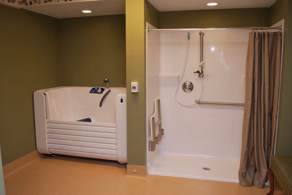 A bathroom with an accessible walk-in bathtub on the left and a walk-in shower with a fold-down seat and grab bars on the right. The walls are painted green and the floor has a beige finish. A beige shower curtain is partially drawn to the side.