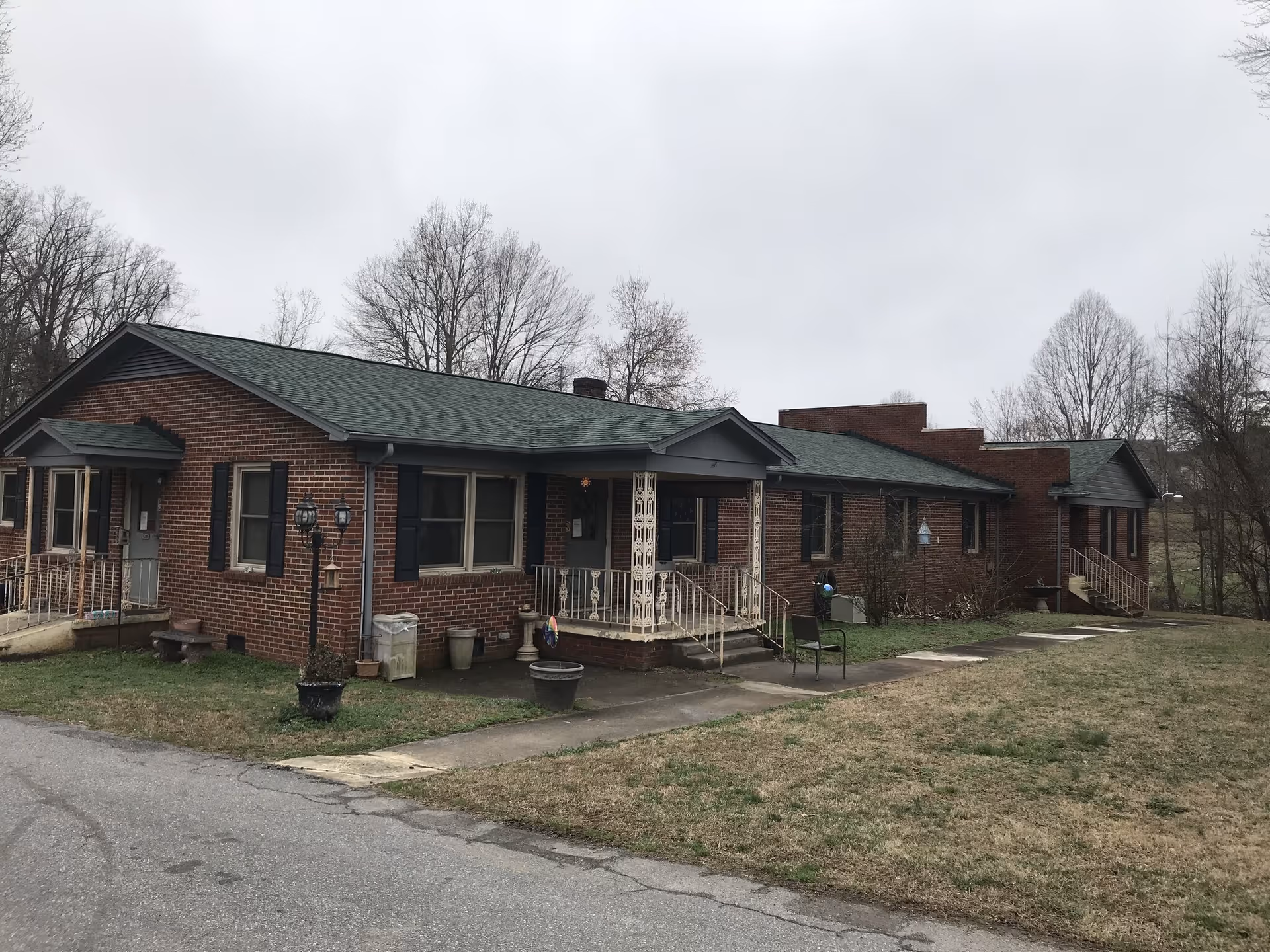 Single-story brick building with a green roof, small porches, and a grassy front yard under an overcast sky.