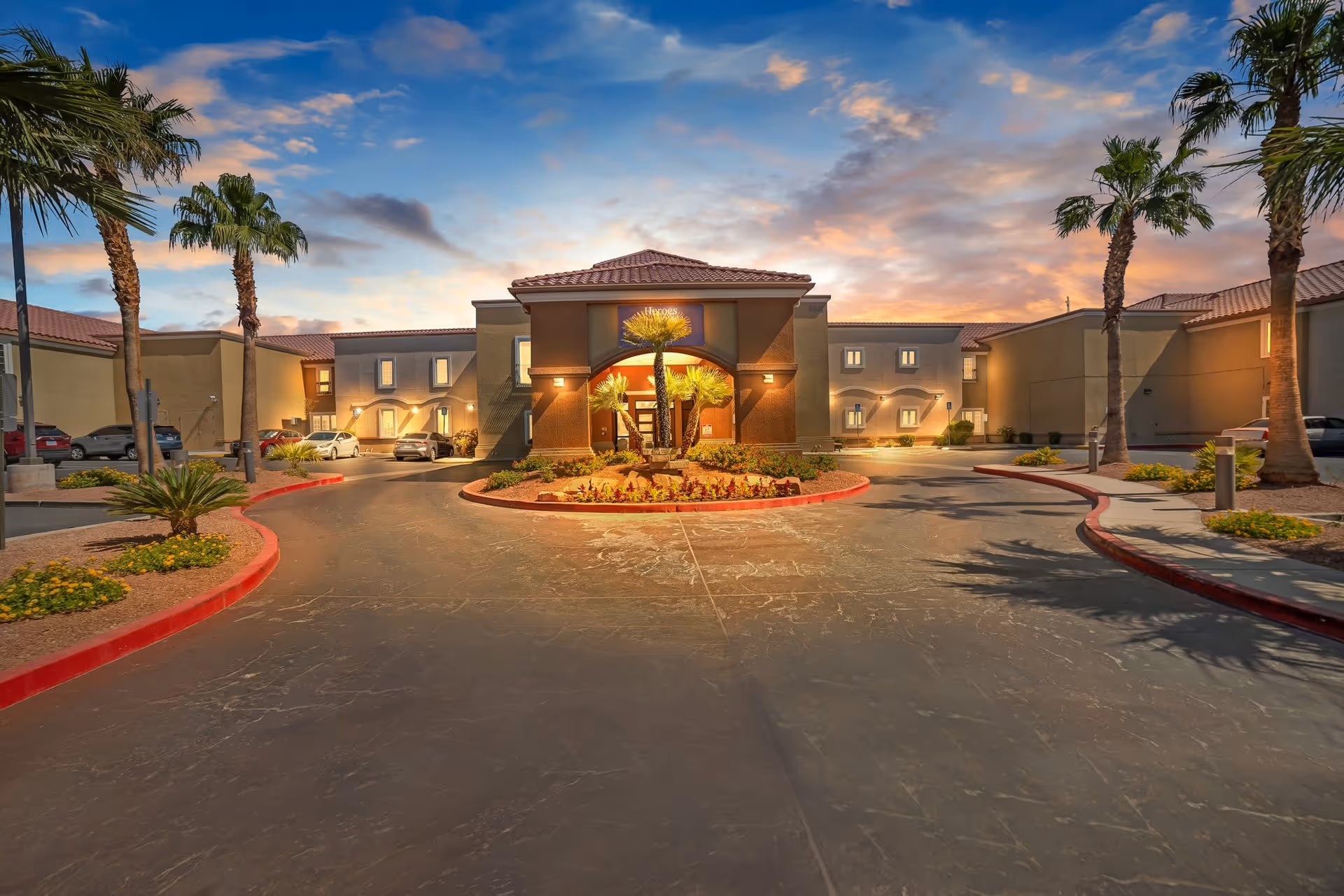 Exterior view of Acacia Springs facility at sunset with a circular driveway, palm trees, and landscaped garden beds in front of the building entrance.