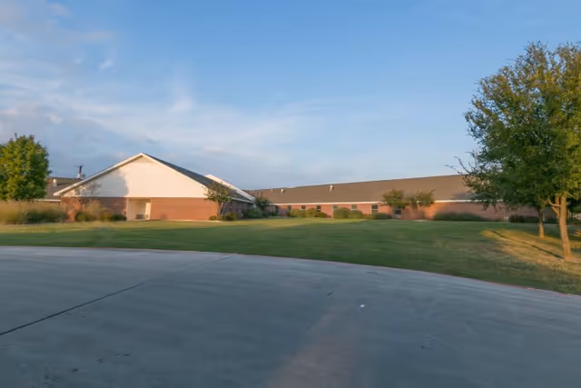 Low, one-story brick healthcare building with a wide green lawn and curved driveway under a blue sky.