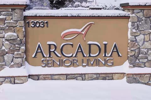Stone and stucco sign for Arcadia Senior Living with the address number 13031, partially covered with snow.