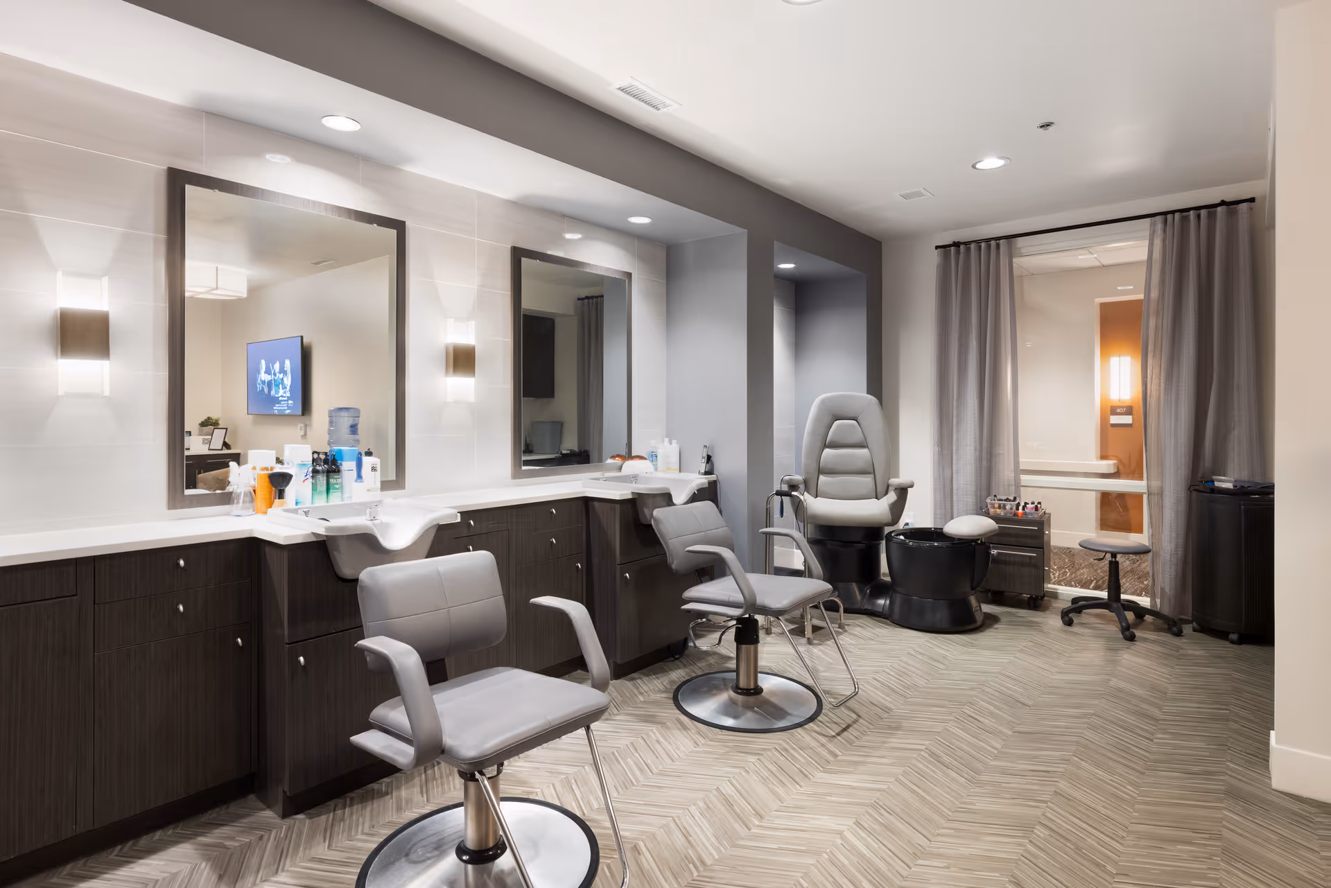 An interior salon with styling chairs, large mirrors, sinks, and a pedicure station.