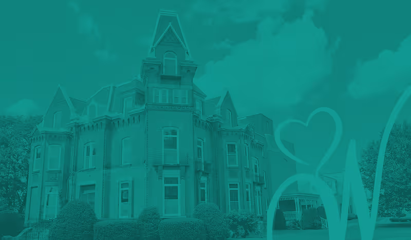 Front view of a large Victorian-style brick building with a central tower, landscaped shrubs, and a teal graphic overlay with a heart.