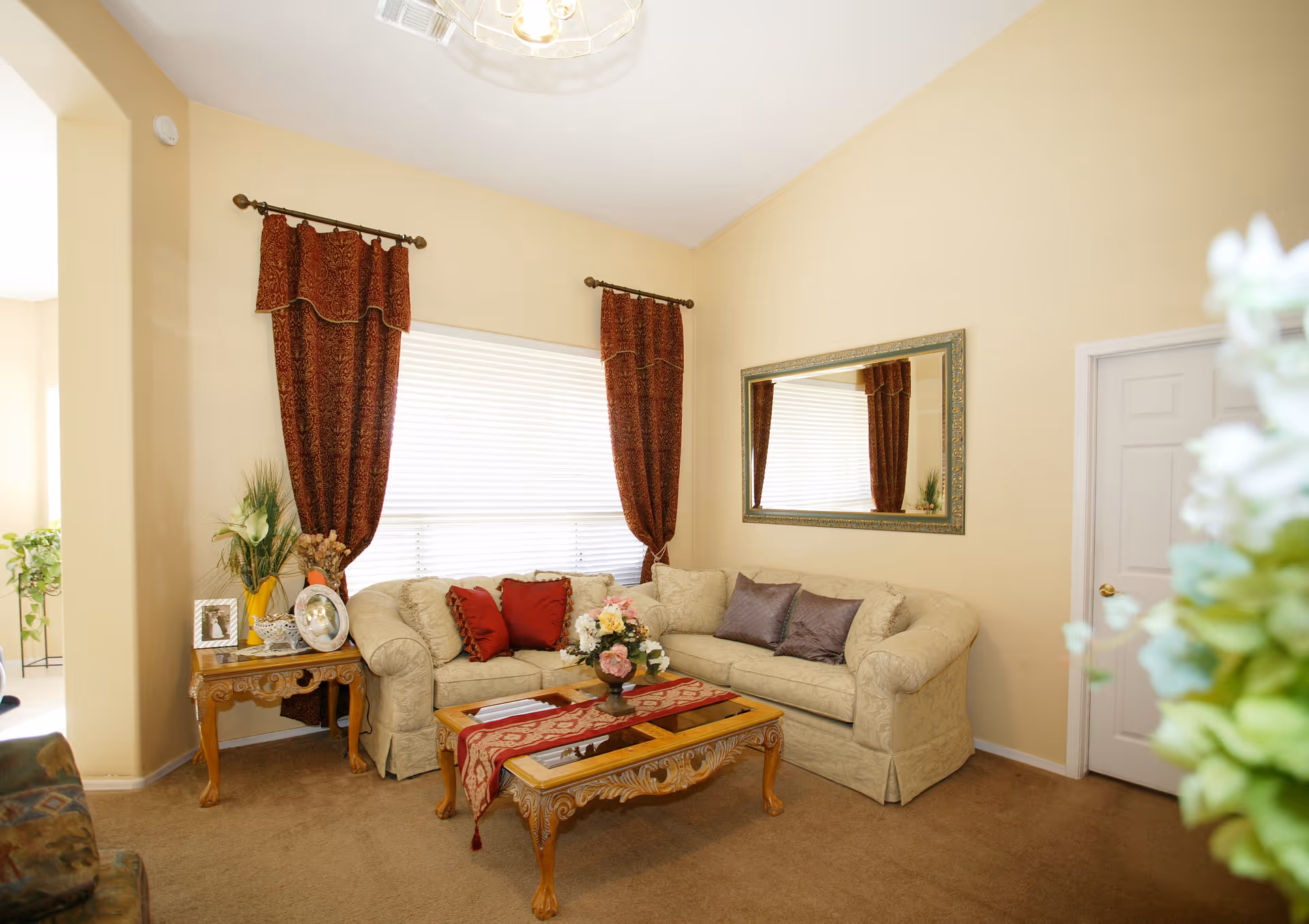 A cozy living room with beige walls, a sofa, decorative curtains, and a coffee table with flowers.