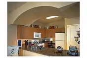 Kitchen with an arched vaulted ceiling and skylight, wood cabinets, white refrigerator, and a countertop island with small appliances and decor.
