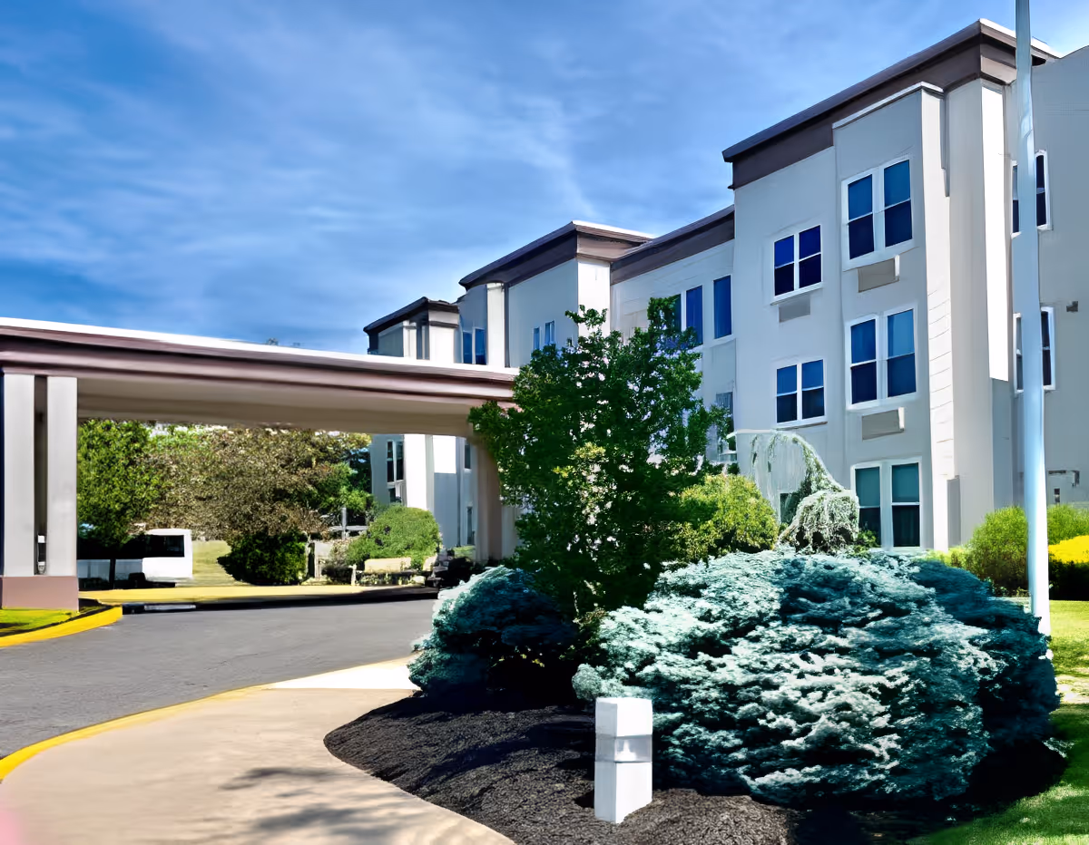 Entrance driveway and landscaped front of a multi-story senior living building with a covered porte-cochere.
