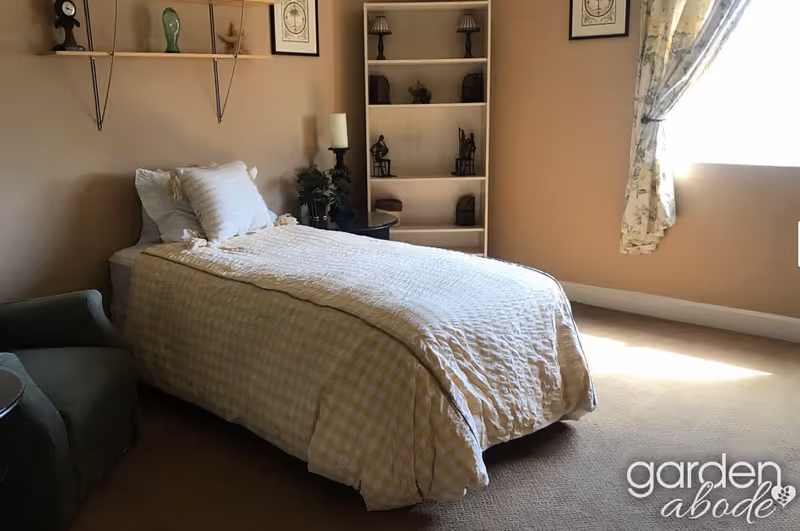 A neatly made bed with a white quilt sits in a cozy bedroom with shelves.