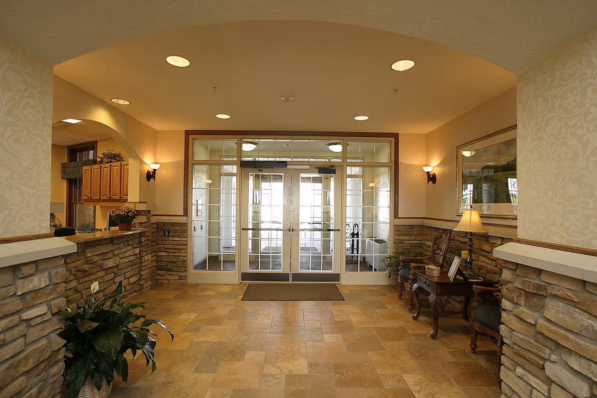 Well-lit lobby with tiled floor, stone half-walls, seating, plants and glass double entry doors.