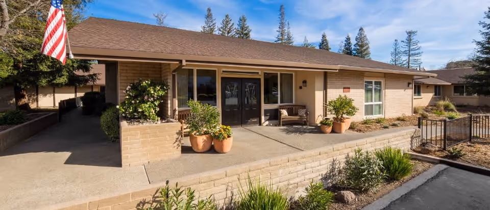 Front view of Manzanita Healthcare Center, a single-story senior living facility with entrance and potted plants.