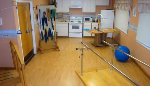 Therapy room with kitchen area, exercise bars, and a blue exercise ball.