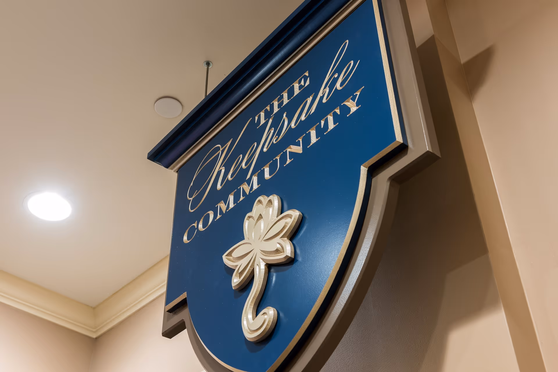 Blue decorative hanging sign with gold lettering and a raised flower emblem mounted on an interior wall.