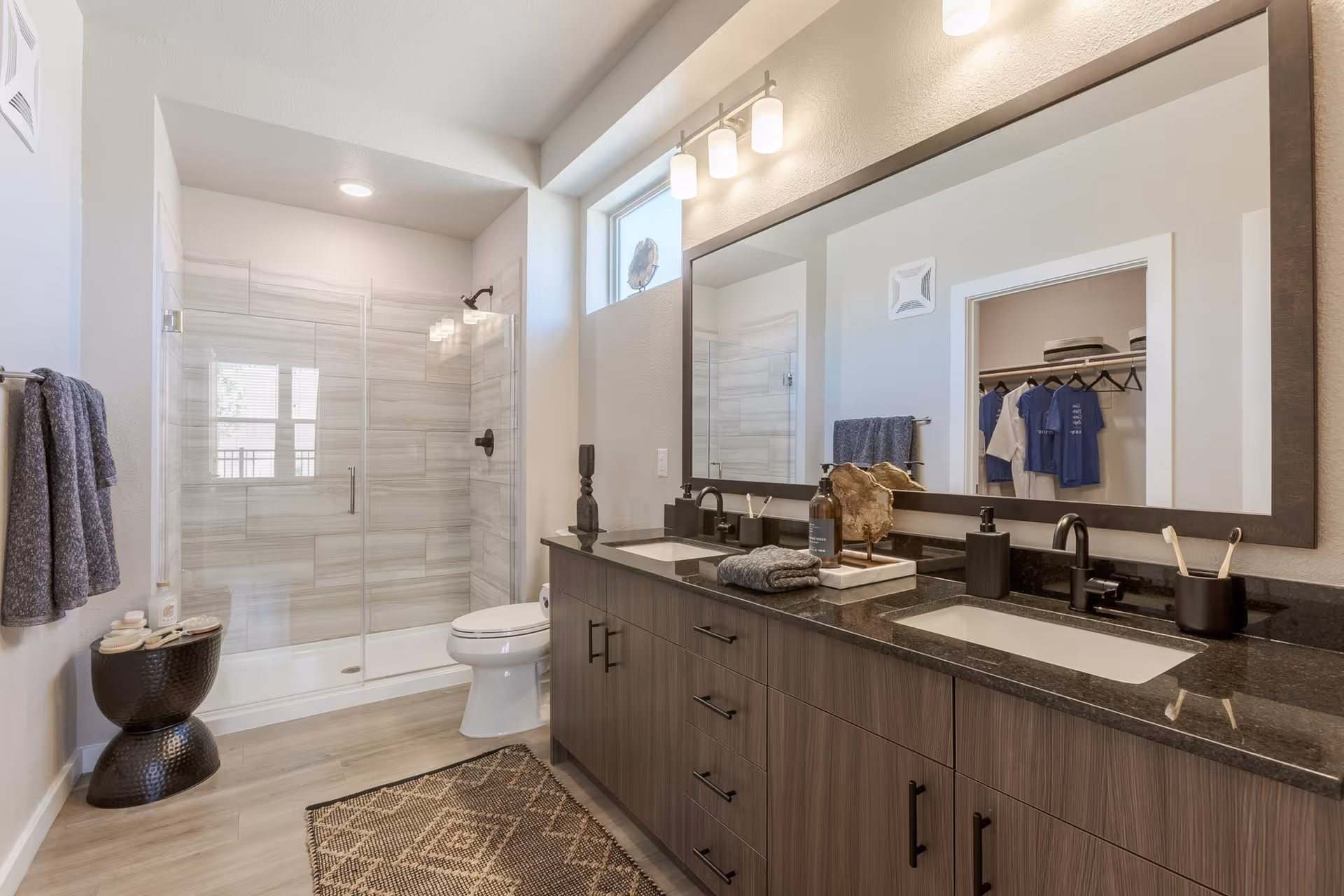 Modern bathroom with a double-sink vanity and large mirror, glass-enclosed walk-in shower and toilet.
