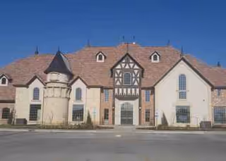 Front exterior view of a two-story stone building with a turret and peaked roof.