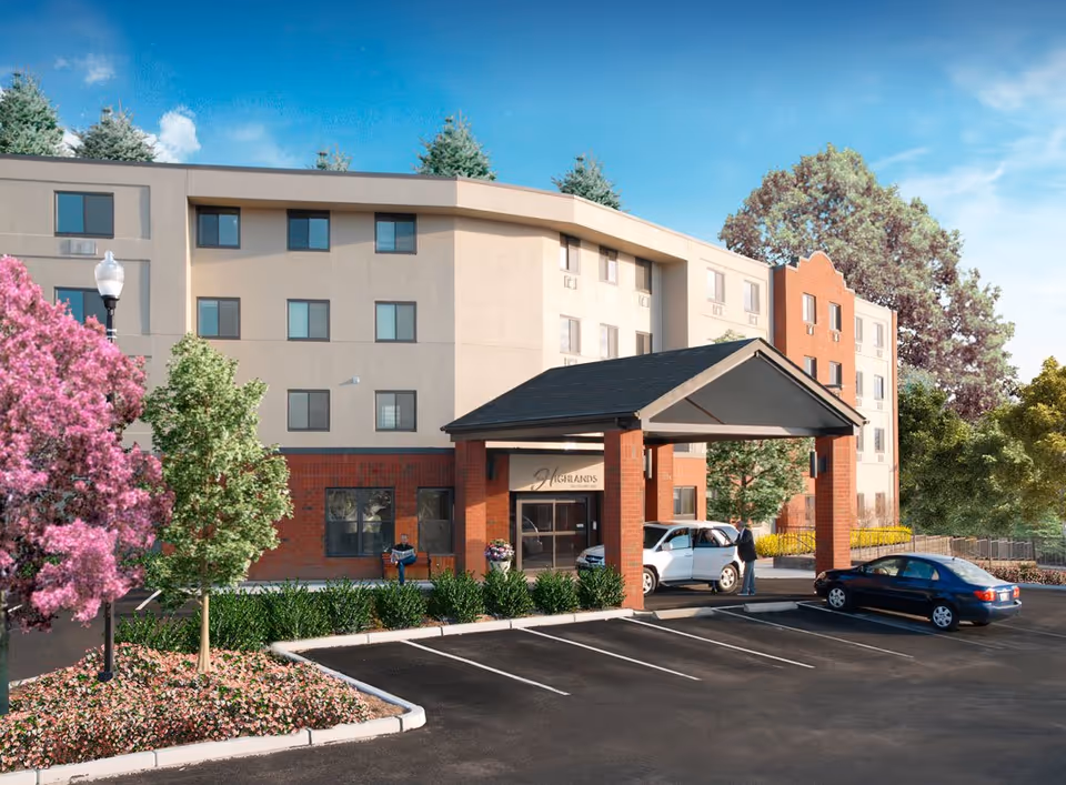 Exterior view of Highlands on the East Side senior living facility showing a multi-story building with a covered entrance. There are two cars parked near the entrance, a person standing by one car, and landscaped areas with trees and flowering plants around the parking lot.