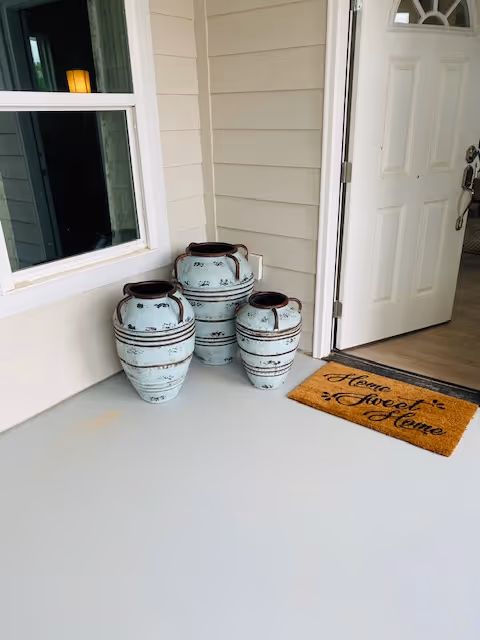 Open front door to a porch with three decorative ceramic pots and a "Home Sweet Home" doormat.