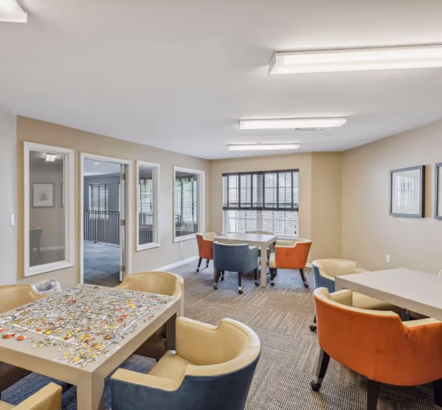 Bright interior common area with tables, colorful chairs, and a puzzle on a table.