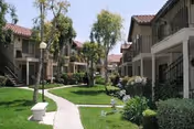 Green courtyard with a paved walkway, trees, and two-story apartment buildings with exterior staircases on either side.