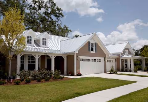 Front view of beige, one story senior living facility with a white garage and manicured lawn.