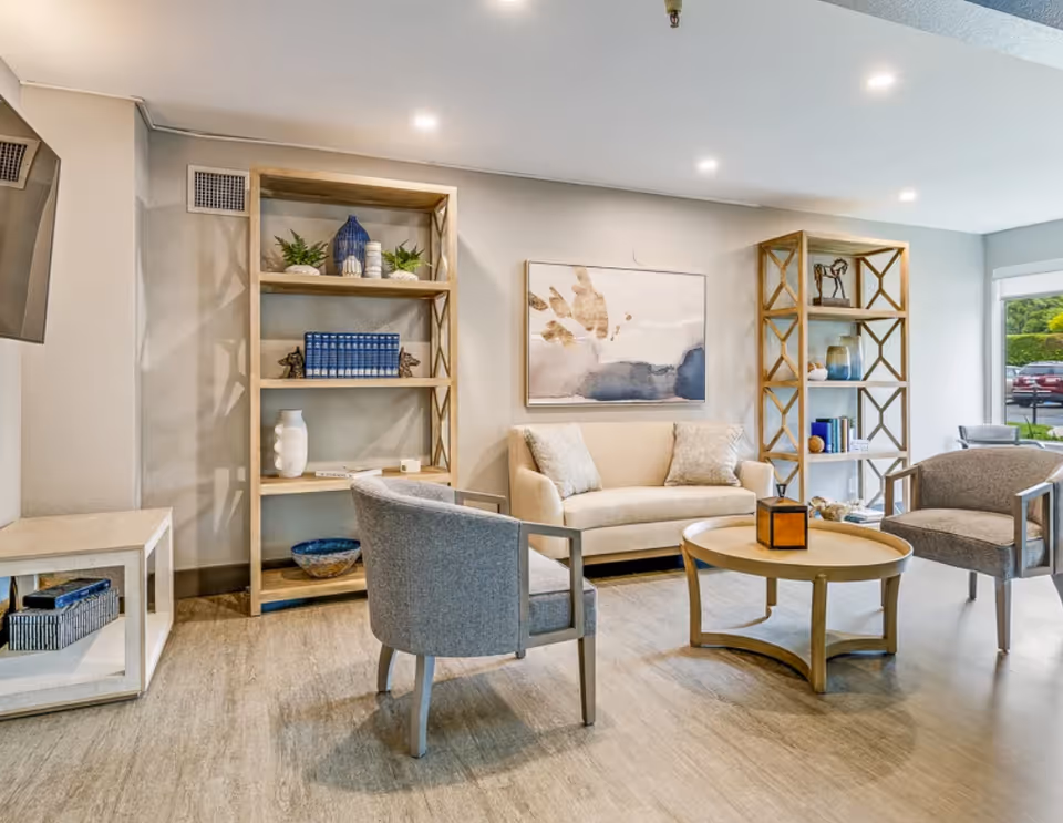 Bright, modern lounge with a sofa, armchairs, round coffee table, and wooden shelving units.